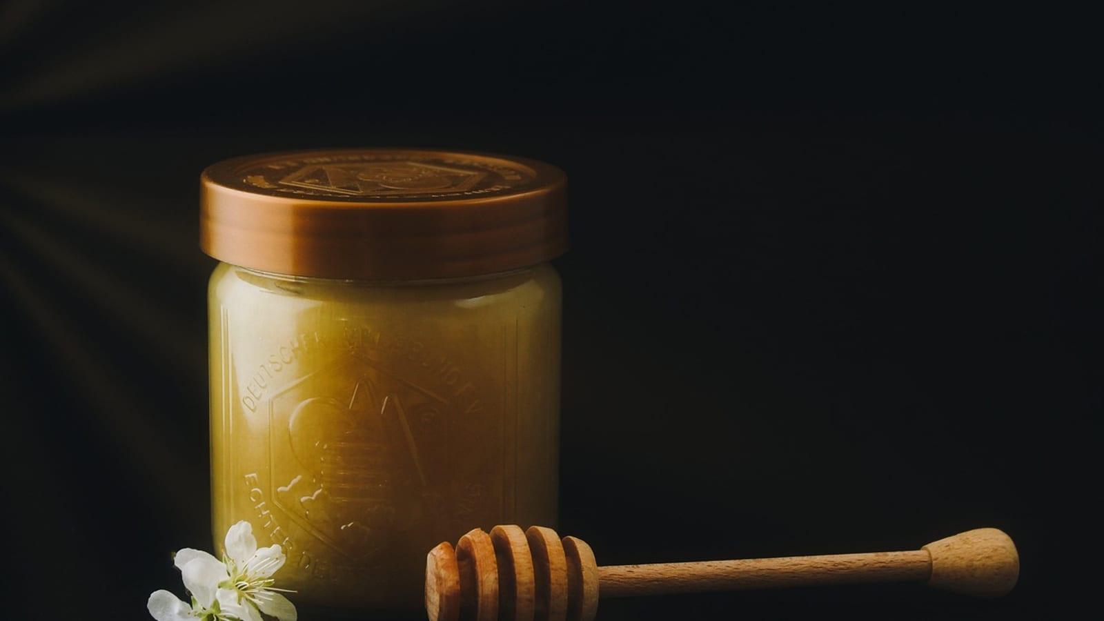 Jar of honey with a wooden dipper on a kitchen table