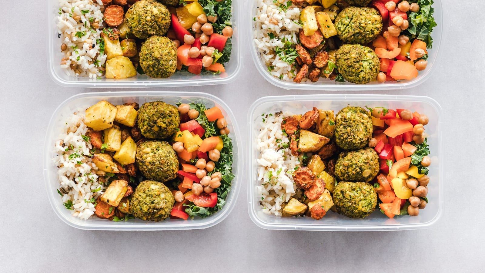 Four glass meal prep containers with grain bowls, roasted vegetables and falafel
