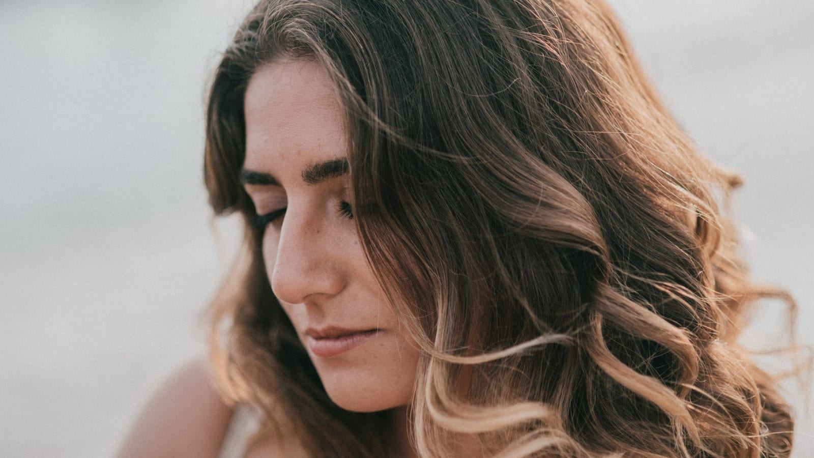 Woman with soft, glossy brown waves looking down in natural light