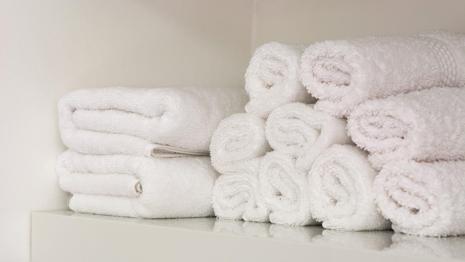 Rolled white towels stacked on a bright white closet shelf