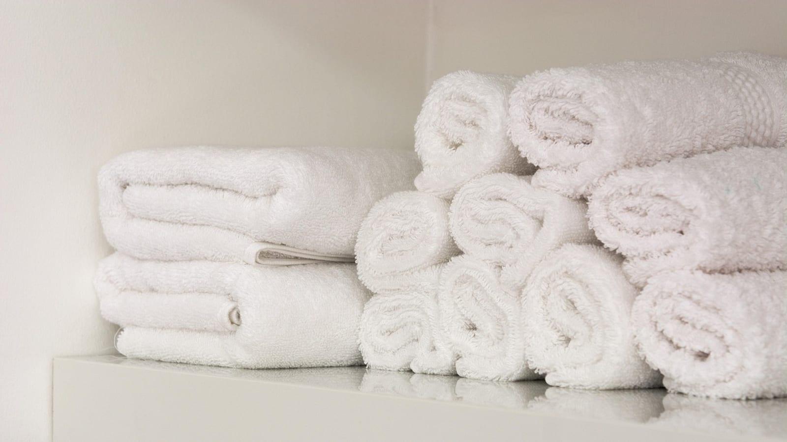 Rolled white towels stacked on a bright white closet shelf