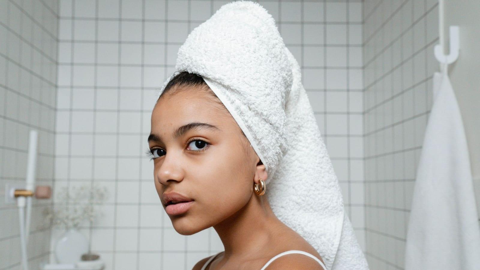 Woman with her hair wrapped on top of her head in a white towel in a tiled bathroom