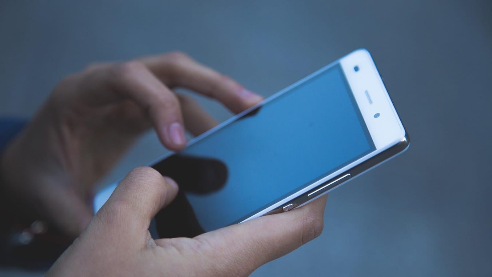 Close-up of two hands holding and tapping a white smartphone