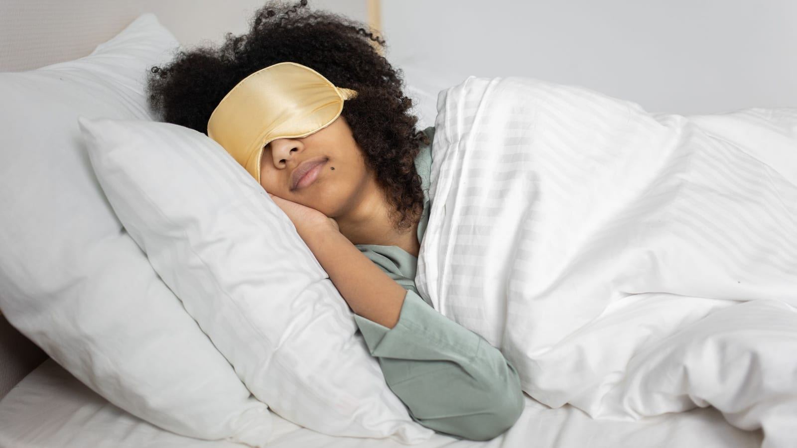 Woman with curly hair sleeping on a white pillow with a satin eye mask