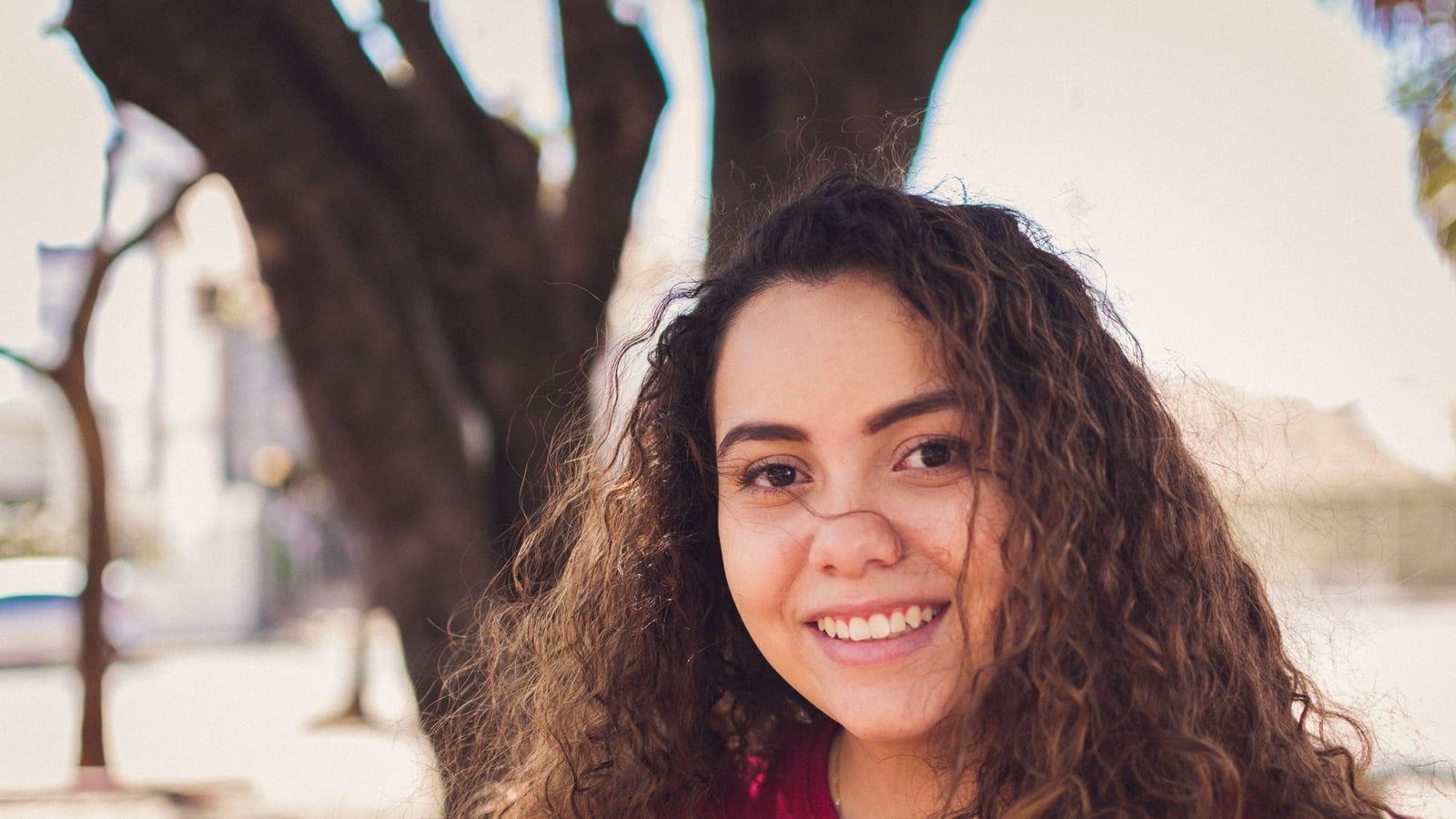 Smiling woman with long, defined brown curls outdoors in natural daylight