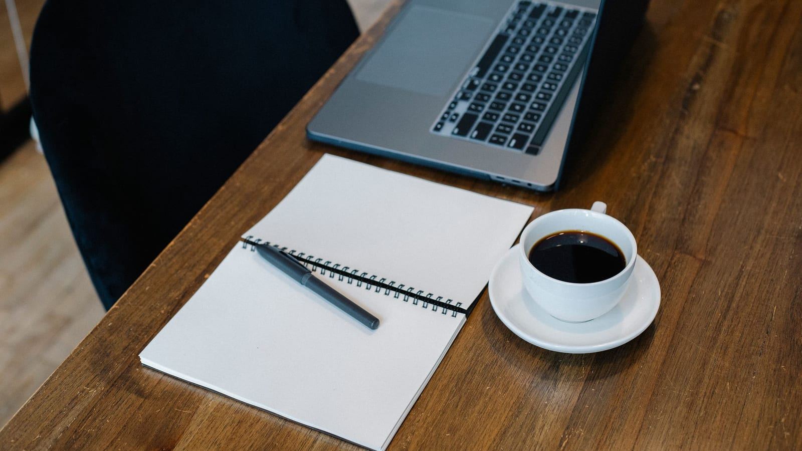 Laptop, notebook and a cup of coffee on a wooden desk