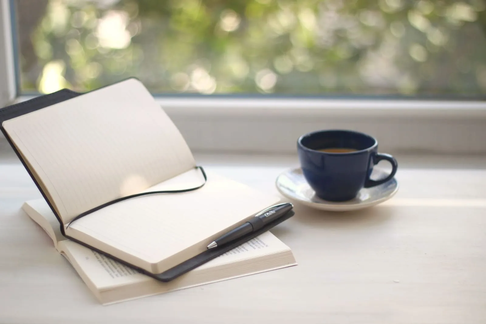 Open journal and a cup of coffee on a sunny windowsill
