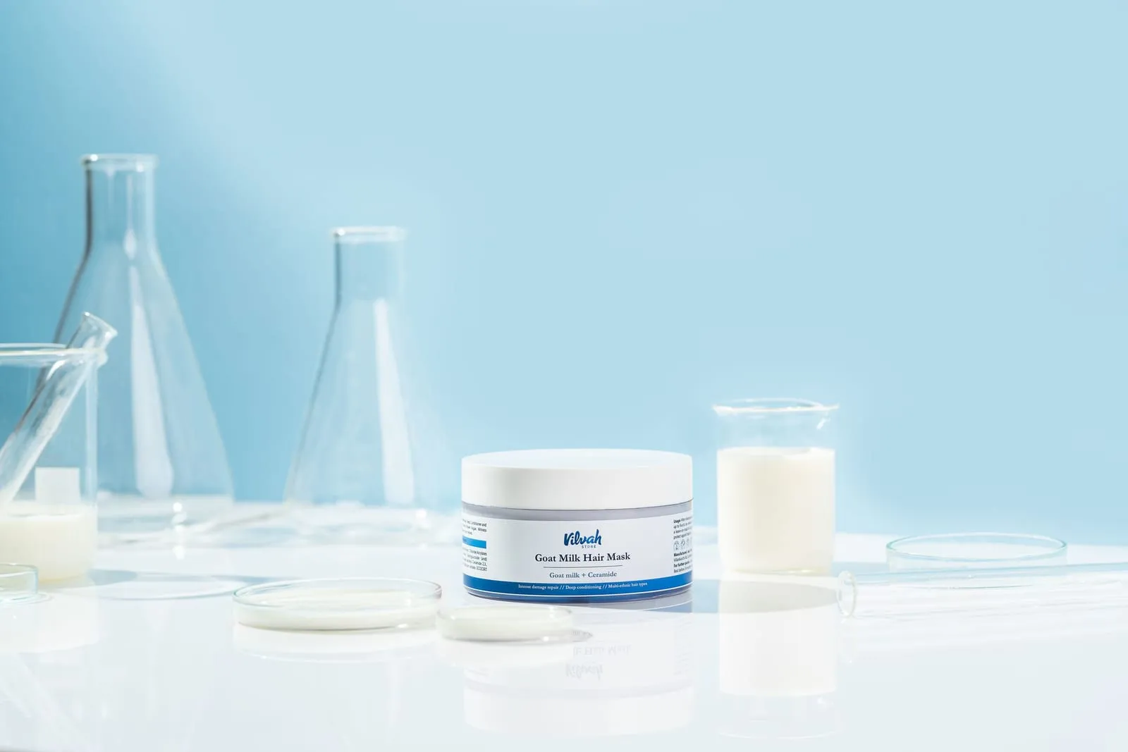 Open jar of hair mask next to laboratory glassware on a light blue background