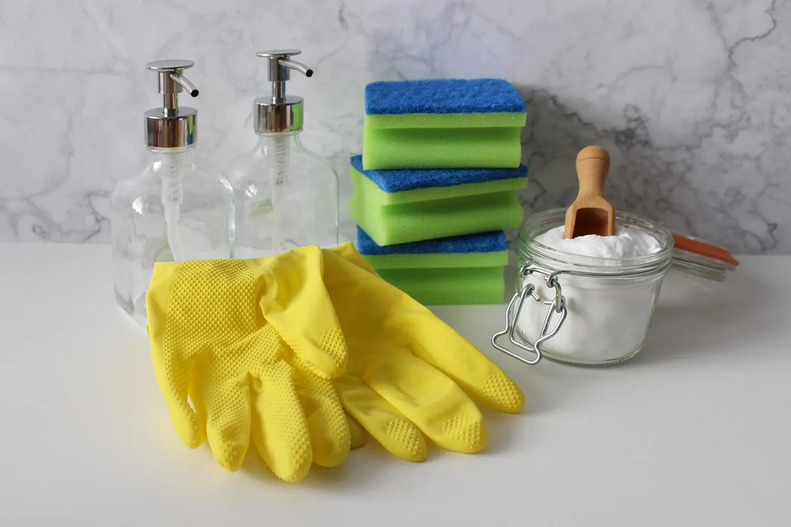 Yellow rubber gloves, sponges, soap dispensers and a jar of baking soda on a white counter