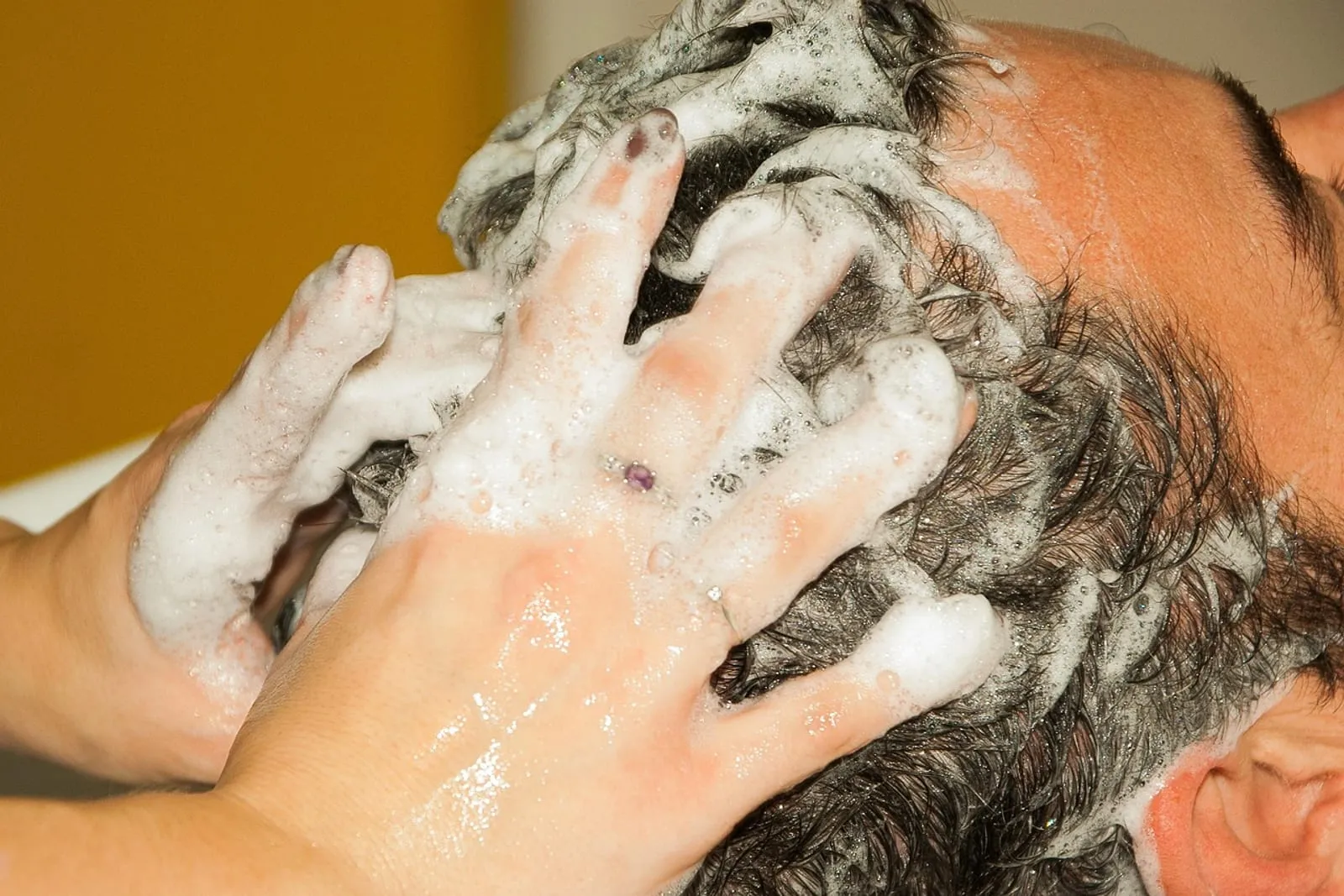 Close-up of a stylist massaging shampoo into a client's hair at the roots