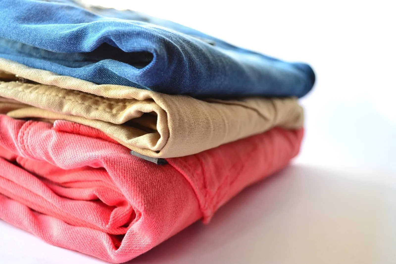 Stack of neatly folded shirts and pants in blue, tan and coral