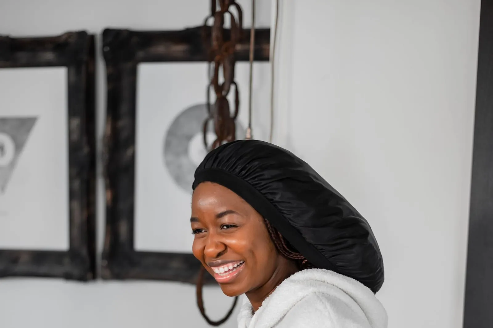 Smiling woman in a black satin bonnet sitting on her bed in the morning
