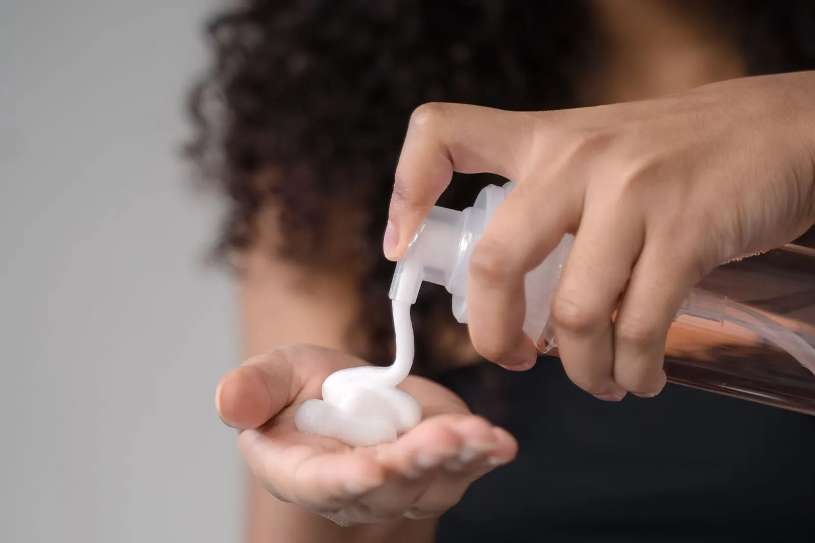 Woman with curly hair pumping a creamy leave-in conditioner into her palm