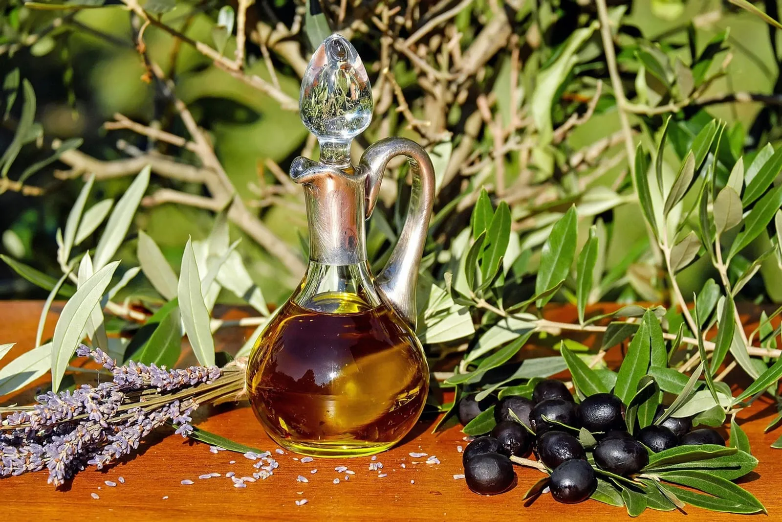 Glass carafe of olive oil surrounded by olive branches