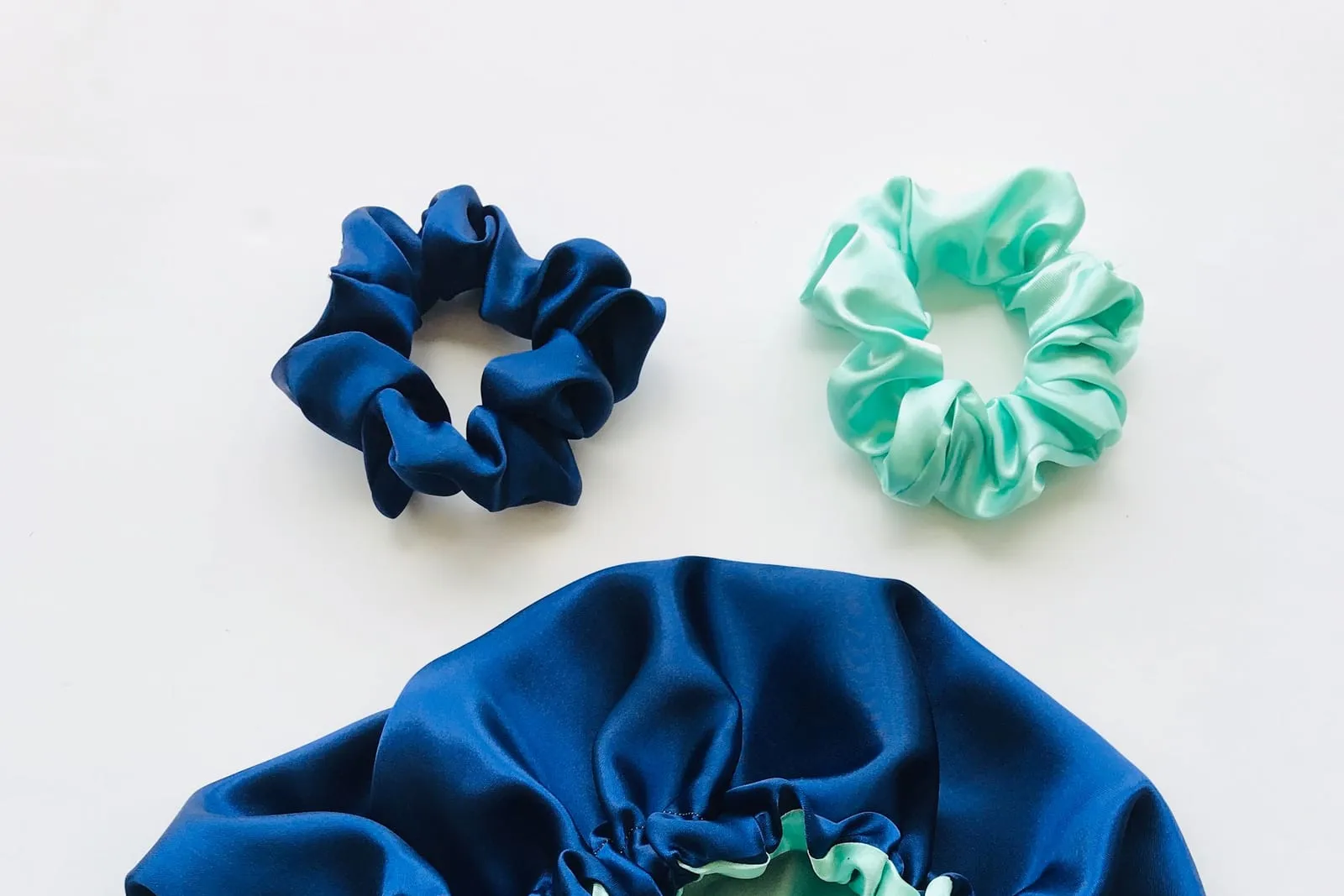 Navy satin bonnet and two satin scrunchies laid flat on a white surface