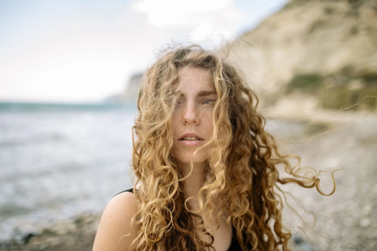 Woman with loose, beachy blonde curls on a windy beach