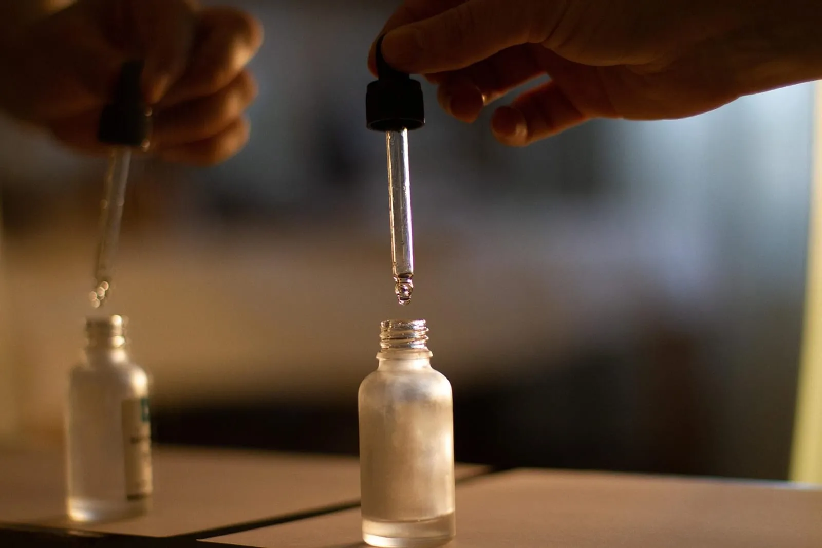 Hands holding glass droppers over small oil bottles