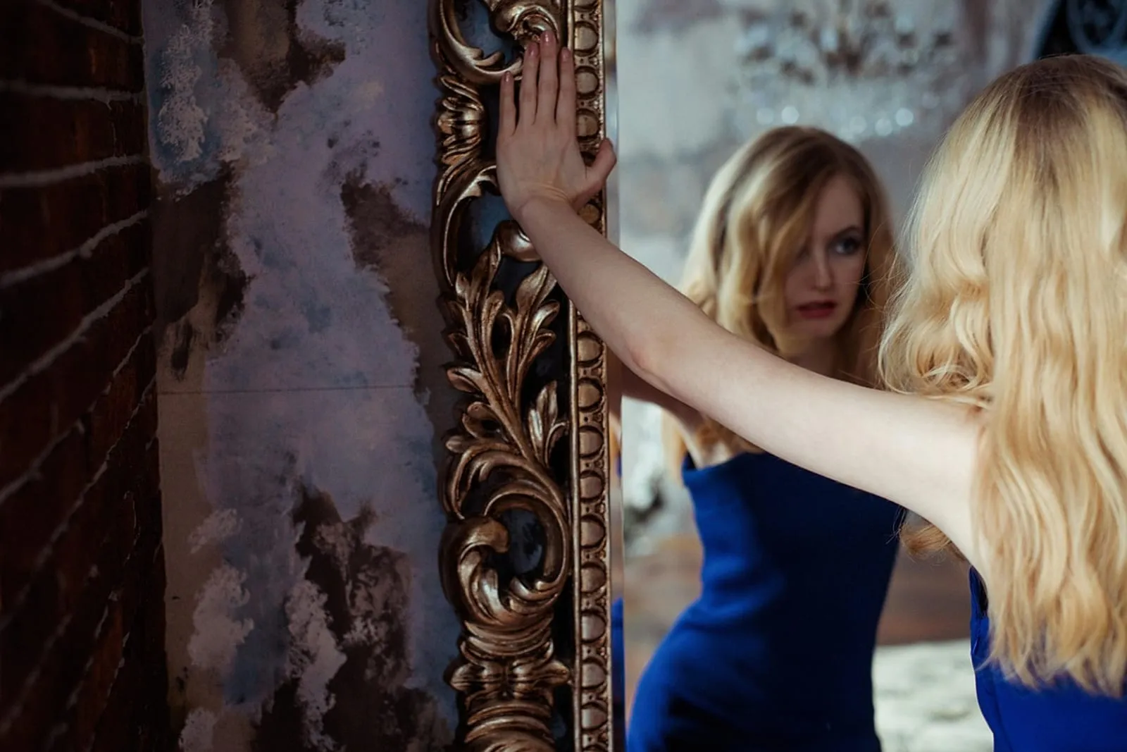 Woman with blonde wavy hair looking at her reflection in a mirror