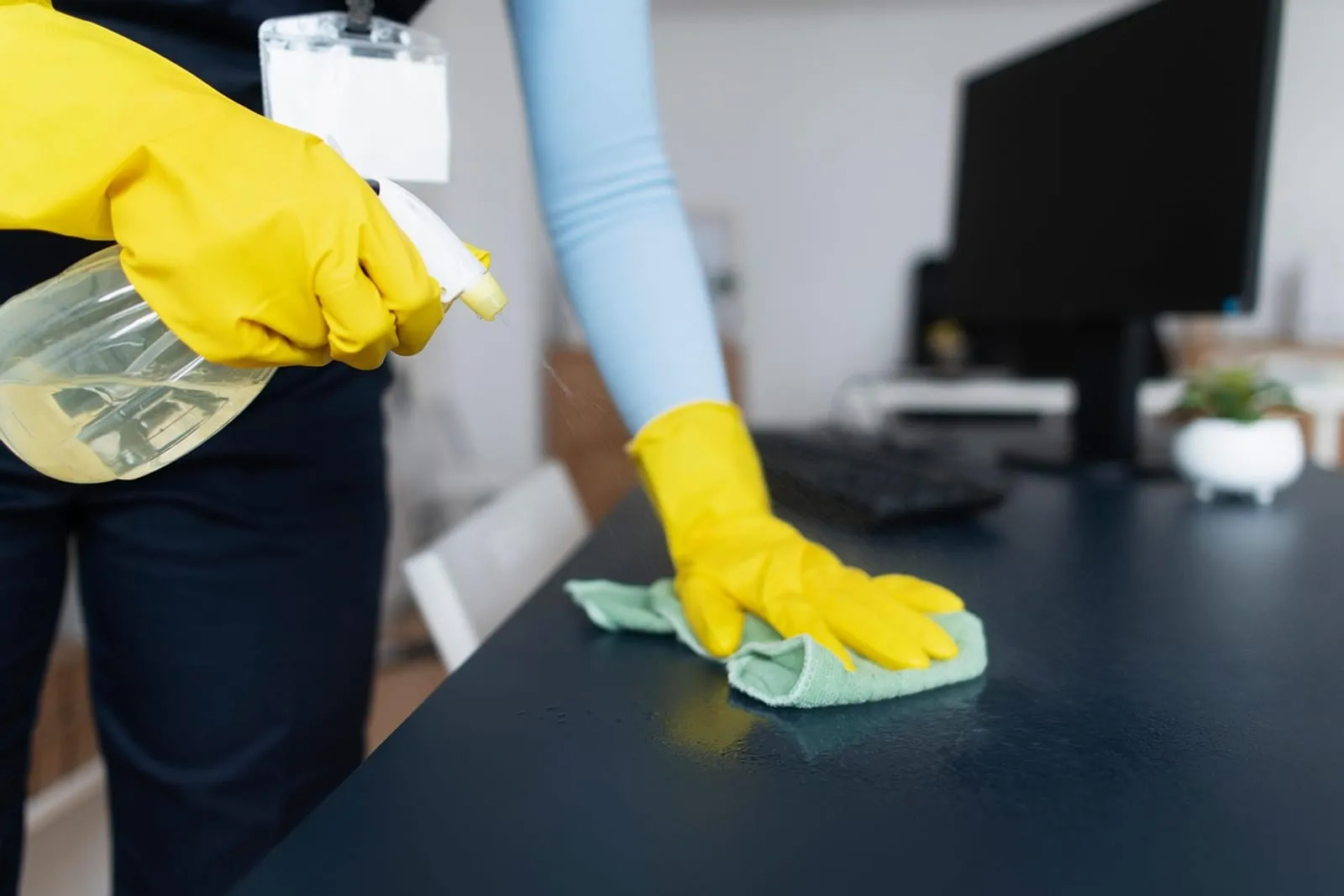 Gloved hand wiping a dark desk with a cloth