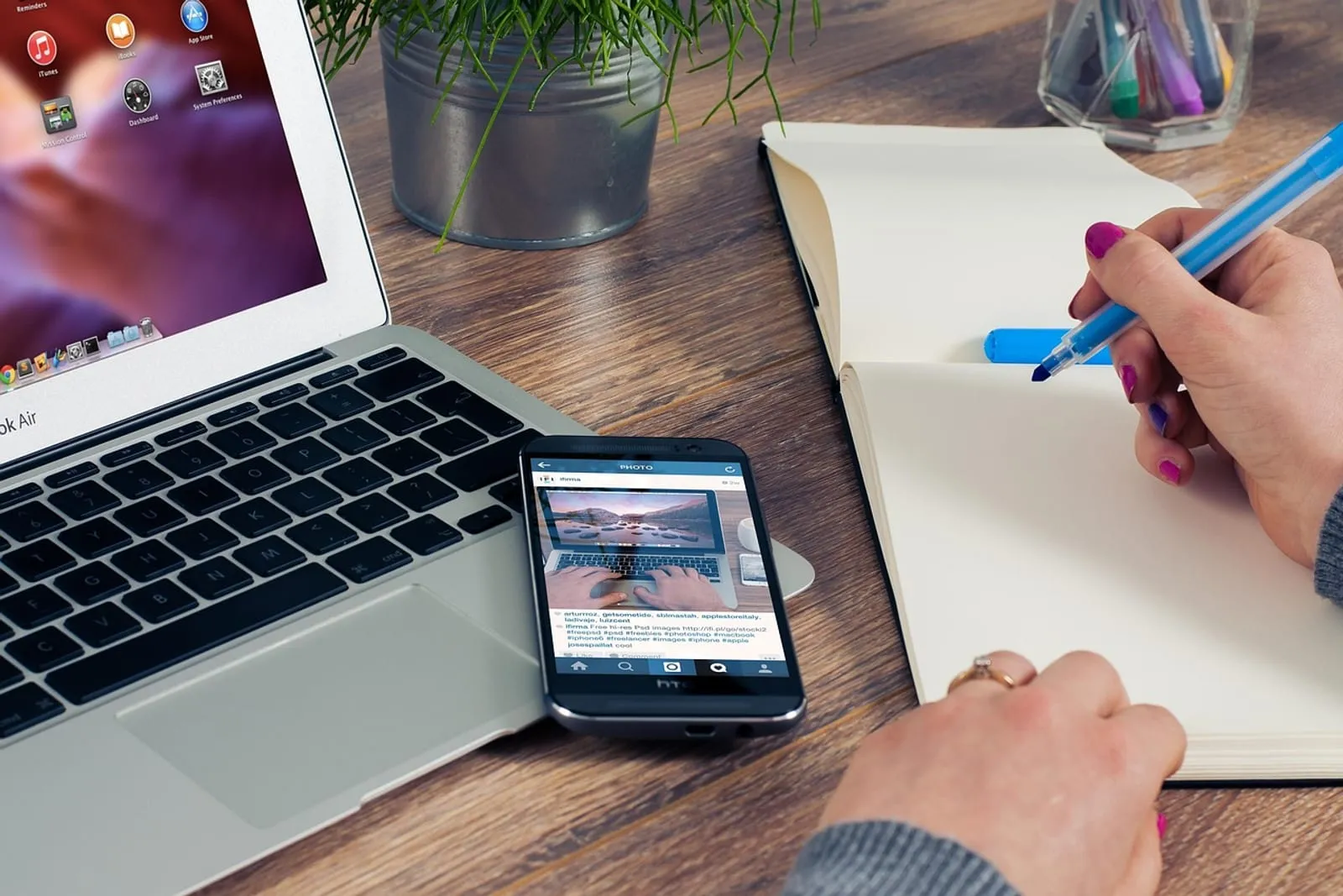 Smartphone and open laptop on a wooden desk while a person writes notes