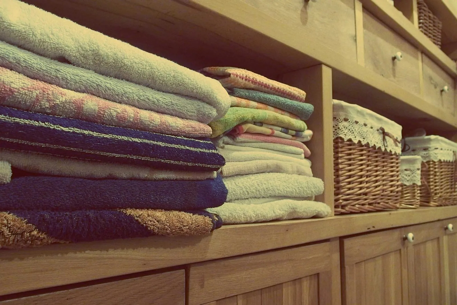 Folded linens and towels stacked on wooden closet shelves with baskets